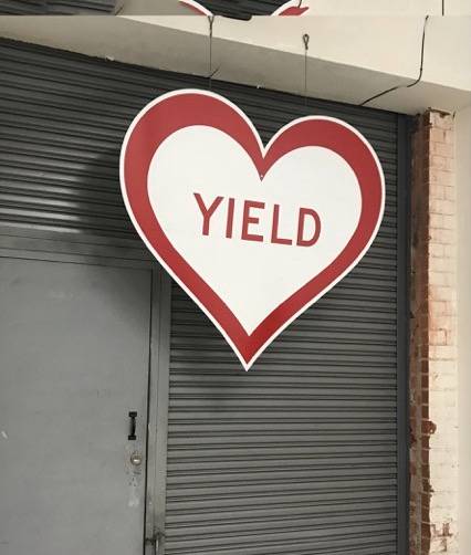 heart shaped sign, white background, red outline text states YIELD